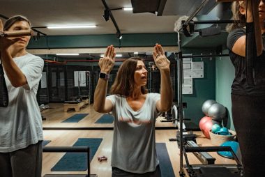 Pilates instructor guiding two women during a workout in a modern gym environment.